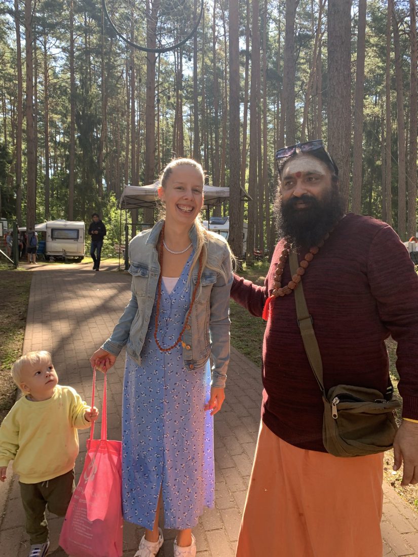 Swami Aditya standing beside Gileta Aadi, his translator, on a sunlit pine-forest path at a gathering